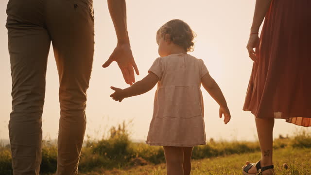 SLO MO Caring Parents Holding Hands of Daughter Walking on Grassy Field under Orange Sky at Sunset
