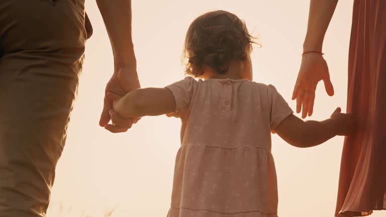 SLO MO Rear View of Caring Parents Holding Hands of Daughter Walking under Orange Sky at Sunset