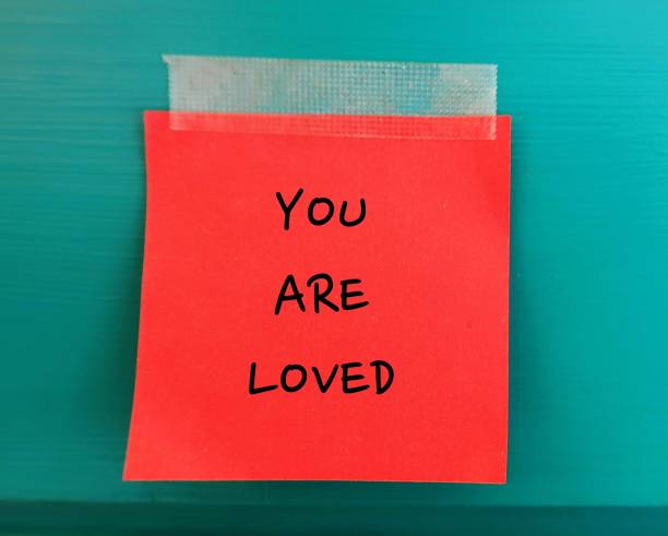 istock Red note on green copy space wall with handwritten text - YOU ARE LOVED - supporttive phrase to encourahe someone else they are loved or positive self talk affirmation 1651937350