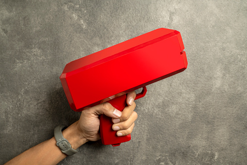 A human hand holding a red money gun on black background