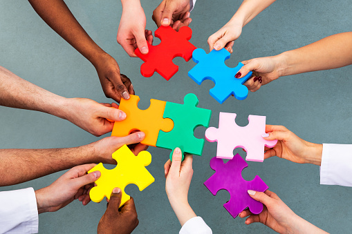 High Angle View Of Medical Team Solving Colorful Jigsaw Puzzle Against Grey Background