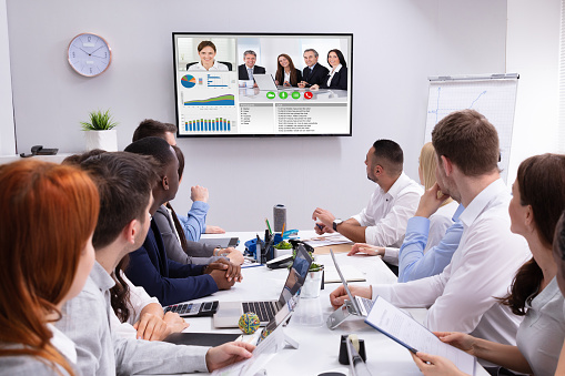Group Of Businesspeople Having Video Conference With Another Business Team In Office