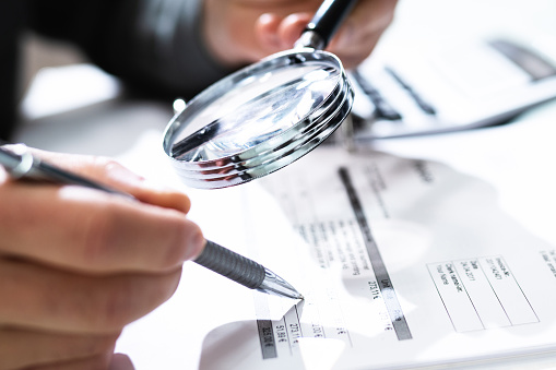 Audit And Fraud Investigation. Auditor Using Magnifying Glass On Document