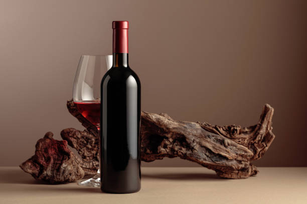 Bottle and glass of red wine with old weathered snag on a beige background. stock photo