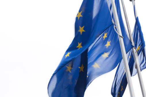 Detail of the national flag of Greece waving in the wind with blurred european union flag in the background on a clear day. Democracy and politics. European country. Selective focus.