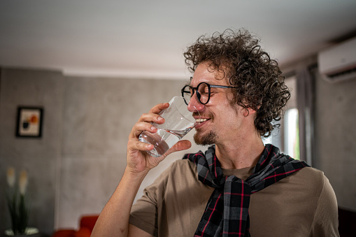 A young man drinks water while sitting at the kitchen island in his apartment, dehydration
