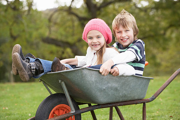 menino e uma menina sentada no carrinho de mão - wheelbarrow playing sibling rural scene - fotografias e filmes do acervo