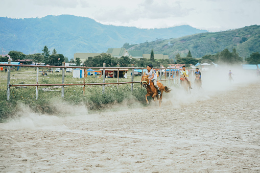 Traditional horse racing in Aceh. Child Jockeys riding horses on the racetrack with mountain background