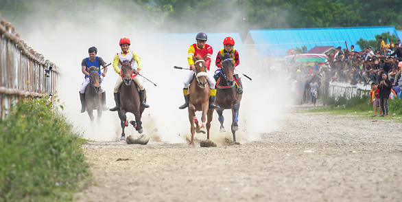 Traditional horse racing in Aceh. Child Jockeys riding and whipping the horses on the dusty racetrack with mountain background