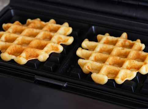 A close-up shot of a waffle maker with two gluten-free homemade waffles inside of it.