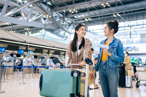 Asian young women passenger walk in airport terminal to boarding gate. Attractive beautiful female tourist friends feeling happy and excited to go travel abroad by airplane for holiday vacation trip.