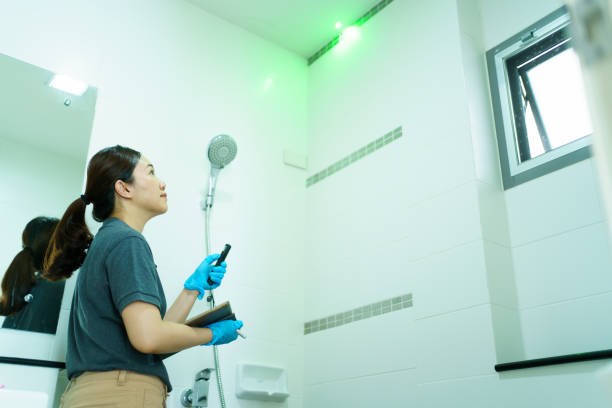 House claim agent inspecting a damaged house. Professional Asian female insurance claim agent using a laser pointer pointing at the damaged ceiling and taking a photo on digital tablet and smartphone, female claim inspector inspecting. Smart Home Water Leak Detection .