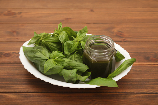 Fresh basil leaves in a white plate and pesto sauce on a wooden background