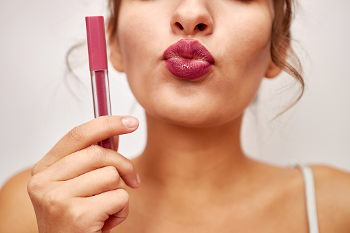 A beautiful girl holds pink lipstick in her hands. Selection and use of cosmetics.