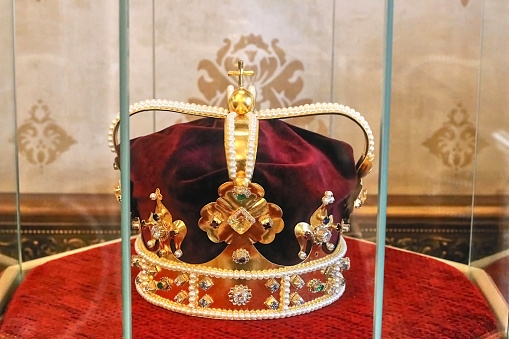 A royal crown, decorated with precious metal and precious stones, stands behind a glass case. Ukraine.