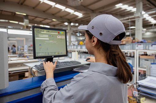 Portrait of apprentice engineering worker young female worker examining and operating CNC plastic injection molding machinery in a factory warehouse after studying manufacturing apprenticeship program certifies