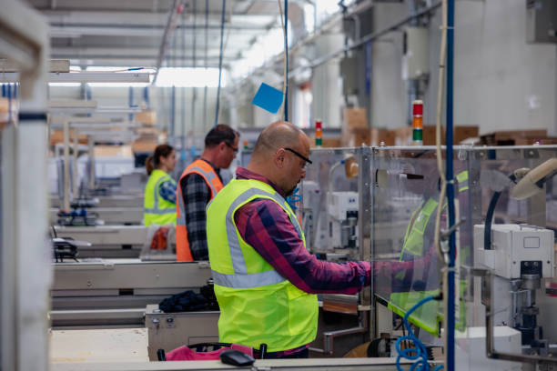 Concentrated professional young industrial factory workers team working with machine parts hands using electric pneumatic screwdriver retractable mechanism, fastened with screws in large Electric electronics wire and cable manufacturing plant factory warehouse