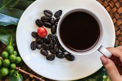 Hand holding white coffee cup with coffee beans on wooden table background