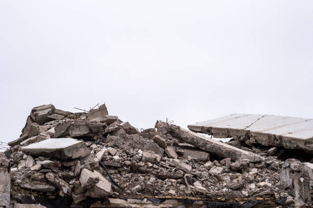 The remains of a destroyed building in the form of a pile of gray concrete debris and construction debris against a gray sky. Background The remains of a destroyed building in the form of a pile of gray concrete debris and construction debris against a gray sky. Background. collapsing stock pictures, royalty-free photos & images