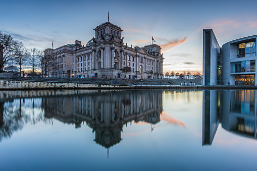 Sunset over the government district in Berlin. Reichstag in the capital of Germany in the evening. River Spree in front of the building with reflections. Slightly reddish clouds in the sky