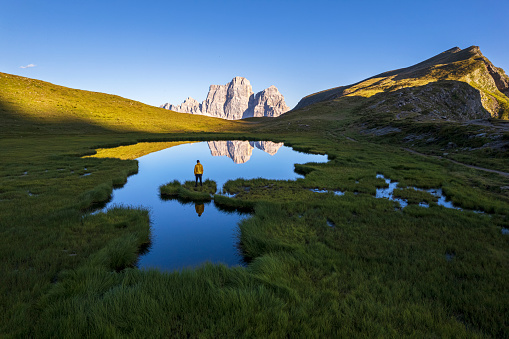 Hiker stands on the shore of the Baste lake reflecting mount Pelmo at sunset, Mondeval, Passo Giau, Trentino Alto Adige - South Tyrol, Dolomites, Italy, Europe