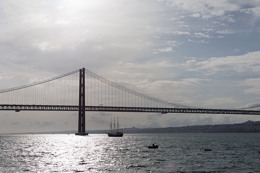 A scenic view of a boat sailing under a bridge on a cloudy day