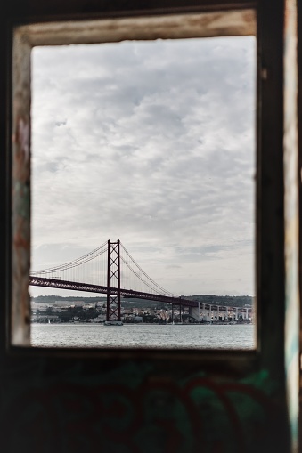 A vertical of a bridge seen through a window on a cloudy day in Ponte, Portugal