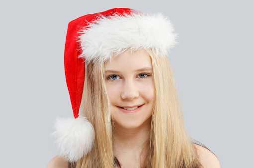Happy Christmas child. Young girl in Santa hat laughing on gray background
