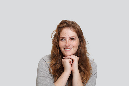 Smiling redhead woman holding her hands near her face on white background, studio portrait