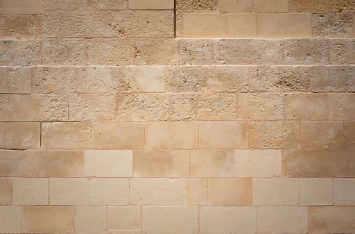Texture and background of a light-colored wall made of large hewn limestone. The wall is brown. The stones are rectangular. The stones are weathered to varying degrees.