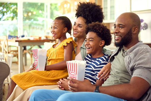 Family Eating Popcorn At Home Sitting On Sofa Together Streaming Show Or Movie To TV