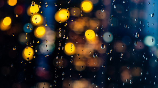 Close-up of illuminated traffic lights and raindrops seen through transparent glass window.