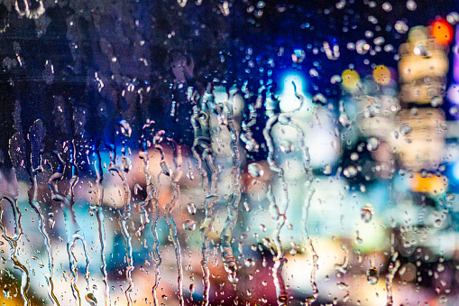 Close-up of illuminated city and raindrops seen through transparent glass window.