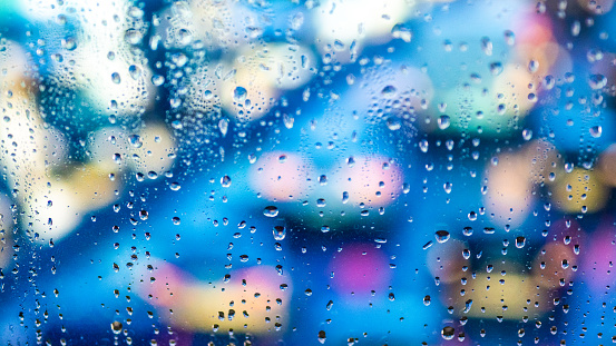 Close-up of illuminated traffic lights and raindrops seen through transparent glass window.