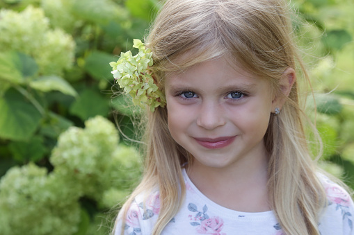 Candid outdoor portrait of happy little girl with green flower behind her ear