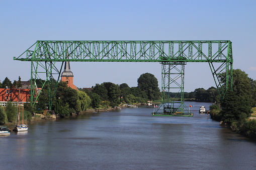 Osten. Germany. Lower Saxonia. Northern Lower Saxonia. The transporter bridge at the village Osten is crossing the Oste River. The steel bridge was build up in 1909. Since 1974 the transporter bridge is a protected technical memorial. It's still working during the summer months for tourists, mainly for ciclyst which are underway in this region. The transporter bridge at Osten is one of two transporter bridges in Germany. The other once is in Rendsburg crossing the Kiel Channel.