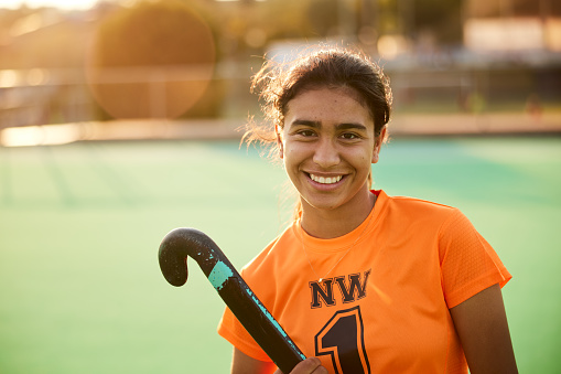 head-shot front view, a teen female hockey player looks at the camera with a cheerful and confident expression, radiating self-assuredness.