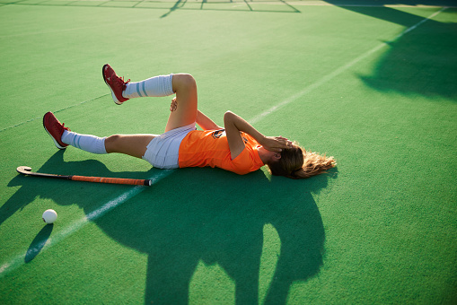 A female hockey player lies on the ground, her face buried in her hands following an injury.