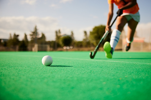 Field hockey ball is in sharp focus in the foreground, with a player and her stick approaching in the background.