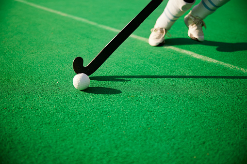 A field hockey player's stick as it interacts with the ball, with the player's identity concealed below the knees