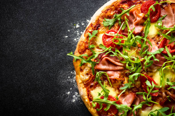istock Traditional italian pizza with ham, cheese, tomatoes and arugula on black. 1652497948