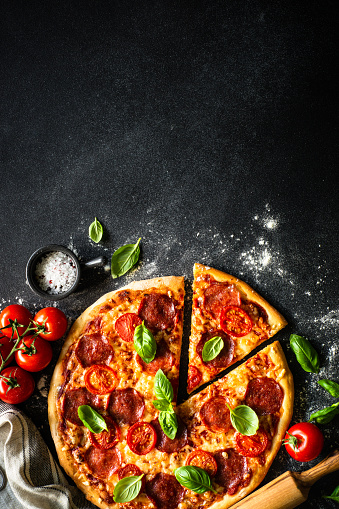Pizza on black background. Traditional italian pizza with salami cheese, tomatoes and basil. Top view, vertical.