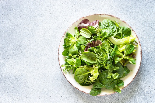 Green salad leaves in white plate at light background. Top view image.