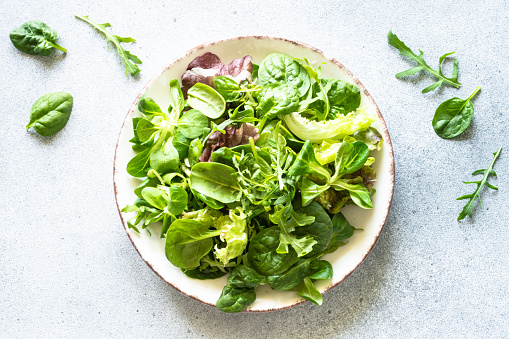 Green salad leaves in white plate at light background. Top view image.