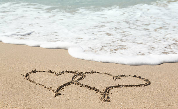 istock Drawing in sand by ocean of two hearts 165250143