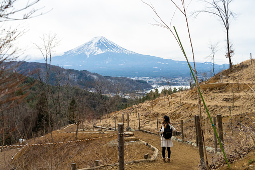 Happy Asian woman travel Japan landmark famous place in winter holiday vacation. Attractive girl enjoy and fun outdoor lifestyle travel nature walking at lake Kawaguchi and Mt Fuji covered in snow.