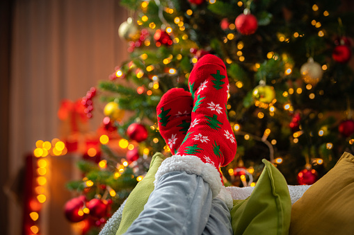 Feet wearing red woolen christmas socks next to Christmas tree