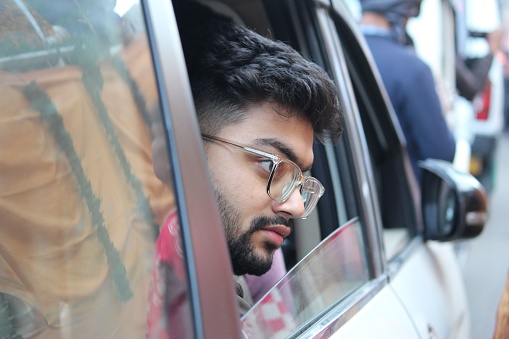 A young South Asian guy with glasses looking out of  window of a car