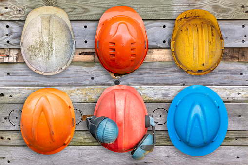 Six colorful old and worn construction helmets hanging on a wooden wall
