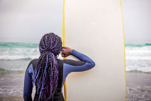 Black Jamaican Surfer Wearing Neoprene View from Back Holding Her Board While Watching the Sea to Catch a Wave